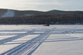 Traces from the wheels of cars lead along the snowy plain of the lake to the fishermen against the background of the coast. Royalty Free Stock Photo