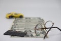 Track of dollar bills. Toy car on a white background with glasses and a calculator, the concept of car ownership cost