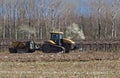 Track tractor with a trailer on a plowed field next to vineyards in the early springtime