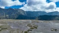 Tracks crisscross Bromo Sea of Sand, leading toward emerald cliffs under a sky of dramatic sunlit clouds Royalty Free Stock Photo