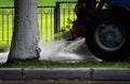 Tractor with a barrel on a trailer pours water over the city sidewalks, powerful streams of water flow down to the ground Royalty Free Stock Photo