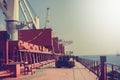 Tractor on cargo ship with bucket and crane for loading. Shipment from a merchant ship to a small ship. Grapple crane fill into