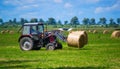 Tractor carrying hay bale rolls and collecting them on a field. Royalty Free Stock Photo