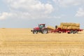 Tractor collecting straw bales during harvesting in the field at nice blue sunny day