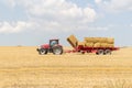 Tractor collecting straw bales during harvesting in the field at nice blue sunny day Royalty Free Stock Photo