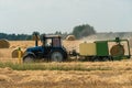 Tractor collects hay bales in the fields. A tractor with a trailer baling machine collects straw and makes round large bales for Royalty Free Stock Photo