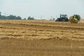 Tractor collects hay bales in the fields. A tractor with a trailer baling machine collects straw and makes round large bales for Royalty Free Stock Photo