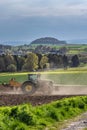 A tractor cultivates a plowed field in the spring