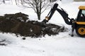 Tractor, excavator digs the earth with a bucket in winter, repairs roads and pipes in the city. Royalty Free Stock Photo