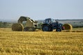 Tractor forming bales of straw. Farmland with blue sky. Harvested wheat field in summer. Copy space. Close-up. Royalty Free Stock Photo