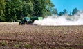 Tractor with a green trailer from which a white powder like dust is spread on the field Royalty Free Stock Photo