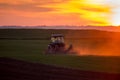 Tractor harrowing field at sunset