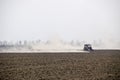 The tractor harrows the soil on the field and creates a cloud of dust behind it