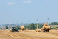 Tractor hauling a round bale an open field with blue sky.