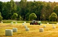 Tractor in a hayfield with bales of hay wrapped in plastic film as fodder for livestock in winter Royalty Free Stock Photo