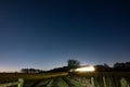 Tractor lights illuminate a path with stars in the night sky above it