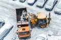 Tractor loader machine uploading dirty snow into dump truck. Cleaning city street, removing snow and ice after heavy Royalty Free Stock Photo