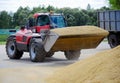 The tractor loads grain into the truck with a large bucket, works in the open air.