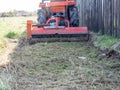 A tractor with a mower attached mulches dry grass along the fence. Land plot processing Royalty Free Stock Photo