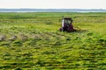 A tractor with a mower mows grass in the lake shore meadows Royalty Free Stock Photo