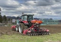 Tractor plows the field in front of some agricultural buildings on a sunny spring day