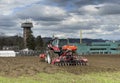 Tractor plows the field in front of some agricultural buildings on a sunny spring day