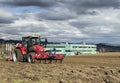 Tractor plows the field in front of some agricultural buildings on a sunny spring day