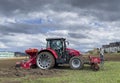 Tractor plows the field in front of some agricultural buildings on a sunny spring day