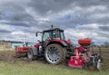 Tractor plows the field in front of some agricultural buildings on a sunny spring day