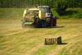 Tractor press hay cuboid on a meadow in front of a corn field Royalty Free Stock Photo