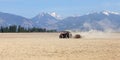Tractor pulling rollers over dry fields in spring, mountains wit Royalty Free Stock Photo
