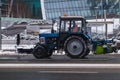 Tractor remove snow from the road. Blue tractor with snowplow and snowblower drive on the street. Winter time street maintenance