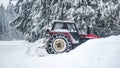 Tractor removing snow from large snowbanks next to forest road, after blizzard in winter