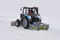 Tractor with a snow plow and a mechanical sweeper moves on a snowy background