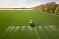 Tractor spraying chemical pesticides with sprayer on the large green agricultural field at spring