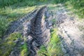 Tractor tire tracks in mud, green grass around, dried up ground in sun Royalty Free Stock Photo