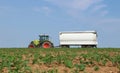 A tractor tows a directional manure spreader on cultivated field with young plants growing