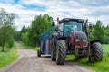 Tractor with trailer on the country side road with green trees and cloudy sky Royalty Free Stock Photo