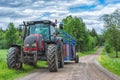 Tractor with trailer on the country side road with green trees and cloudy sky Royalty Free Stock Photo