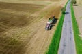 A tractor with a trailer full of manure scatters organic fertilizer on a field near a country road, aerial view.