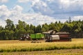 Tractor and trailer moves in a field with working combine harvester