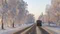 Tractor with trailer on a picturesque rural road at sunset. On the sides of the road there are beautiful trees in frost.