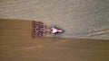 A tractor with a trailer plough plows a farmer\'s field from a aerial view. Top view of working rural machinery Royalty Free Stock Photo