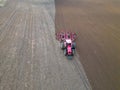 A tractor with a trailer plough plows a farmer\'s field from a aerial view. Top view of working rural machinery Royalty Free Stock Photo