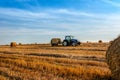 A tractor uses a trailed bale machine to collect straw in the field