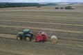 A tractor uses a trailed bale machine to collect straw in the field and make round large bales. Agricultural work, baling, baler,