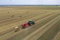 A tractor uses a trailed bale machine to collect straw in the field and make round large bales. Agricultural work, baling, baler,