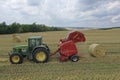 A tractor uses a trailed bale machine to collect straw in the field and make round large bales. Agricultural work, baling, baler,