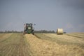 A tractor uses a trailed bale machine to collect straw in the field and make round large bales. Agricultural work, baling, baler,