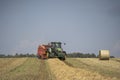 A tractor uses a trailed bale machine to collect straw in the field and make round large bales. Agricultural work, baling, baler,